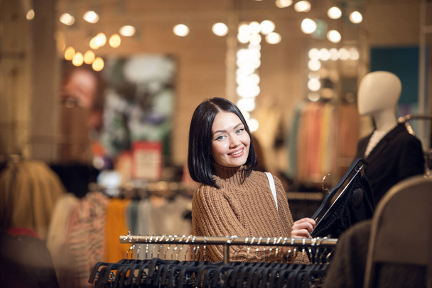 Młoda uśmiechnięta dziewczyna kupuje ubrania w centrum handlowym, patrząc - Zdjęcie, obraz
