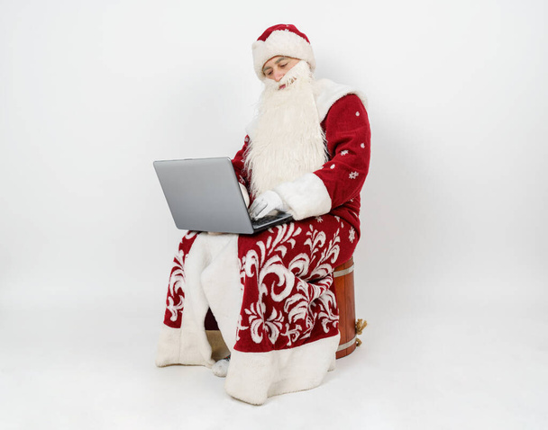 Christmas and New Year concept. Santa Claus sits at his desk and works at the computer. - Фото, зображення