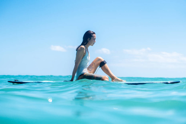 Portrait of surfer girl on surf board in blue ocean pictured from the water in Bali - Photo, image