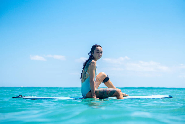 Portrait of surfer girl on surf board in blue ocean pictured from the water in Bali - Photo, Image