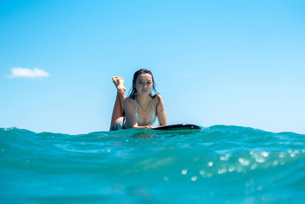 Portrait of surfer girl on surf board in blue ocean pictured from the water in Bali - Фото, изображение