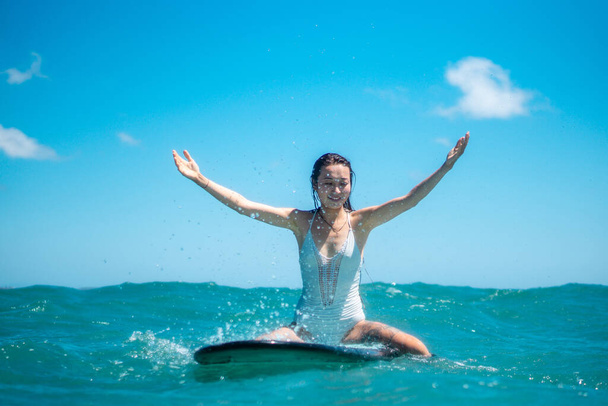 Portrait of surfer girl on surf board in blue ocean pictured from the water in Bali - 写真・画像
