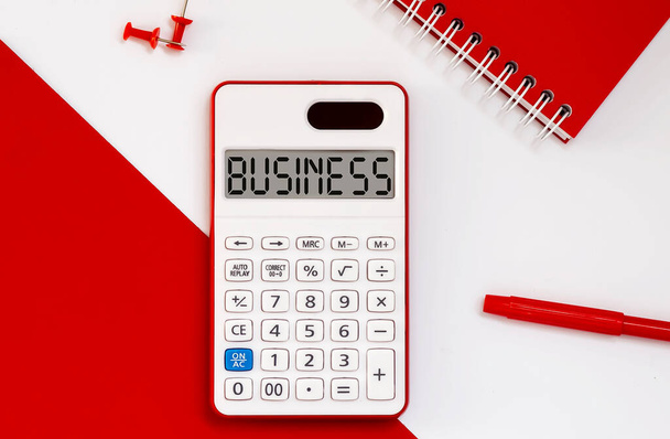 calculadora con la palabra NEGOCIO en pantalla con bloc de notas rojo y herramientas de oficina - Foto, imagen