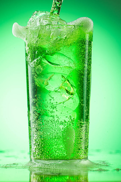 pouring green tarragon lemonade into glass with pieces of pure real ice on green gradient background - Φωτογραφία, εικόνα