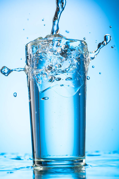 pour clear water into a glass with chunks of pure real ice on a blue gradient background - Fotografie, Obrázek