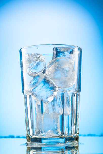 pour clear water into a glass with chunks of pure real ice on a blue gradient background - Фото, изображение