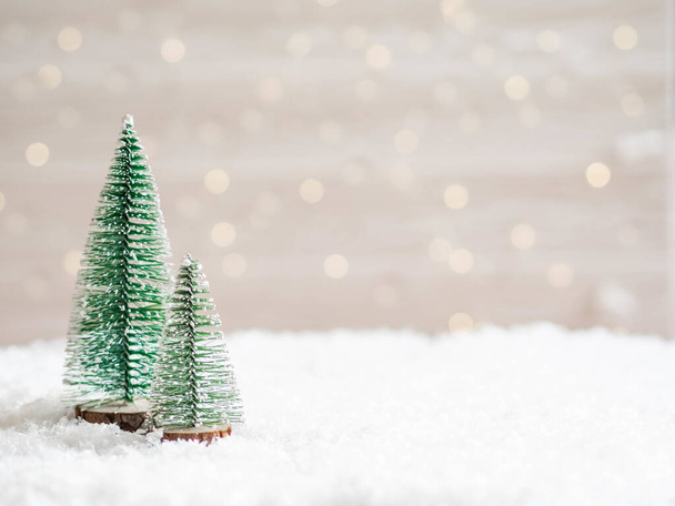Christmas trees in the foreground in artificial snow and a blurred background with a glowing garland. Copy space. Front view. Minimal blurred background - Photo, Image