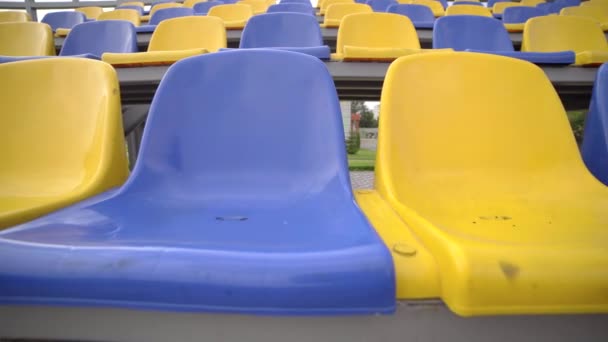 4k, lege plastic stoelen in het stadion. Rijen van gele en blauwe stoelen in voetbalstadion Tribune zonder toeschouwers en fans - Video