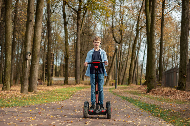 A boy on a Segway rides through the autumn park alone. - Foto, afbeelding