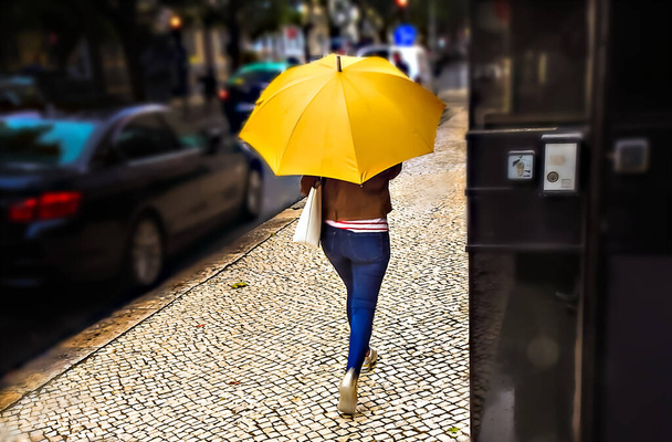 Sylwetka kobiety z żółtym parasolem chodzącej po brukowanej ulicy - Zdjęcie, obraz