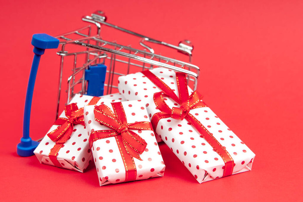 An overturned grocery cart full of gifts on a red background with copy space.  Concept for christmas, holidays, discounts and shopping. - Фото, зображення