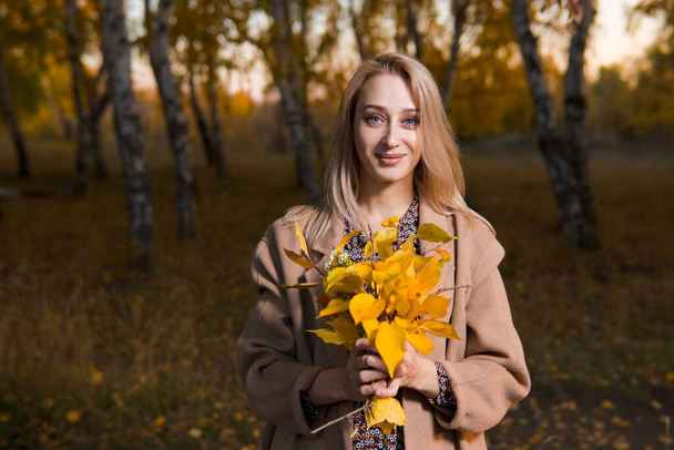 Nuori kaunis nainen pitkä takki keltainen lehdet poseeraa syksyllä metsässä.  - Valokuva, kuva