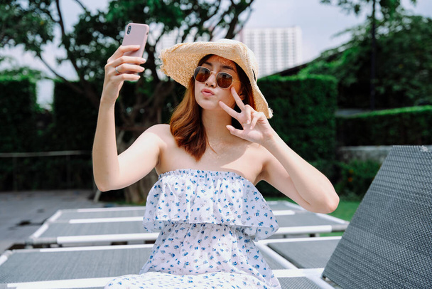 美しいアジアの女性旅行者は帽子とサングラスを身に着けています自己撮影とともにスマートフォン. - 写真・画像