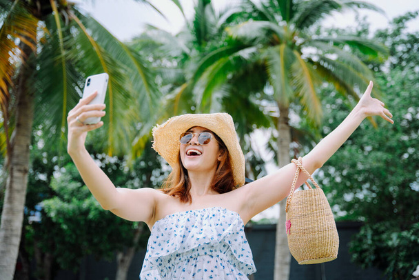 美しいアジアの女性旅行者は帽子とサングラスを着用します旅行vlogとともにスマートフォン. - 写真・画像