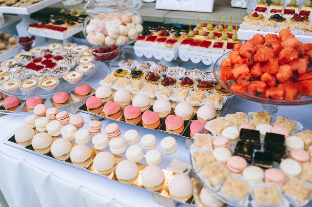 Wedding candy bar with different colored bright cupcakes, macaroons, cakes, jelly and fruits. - Foto, Bild