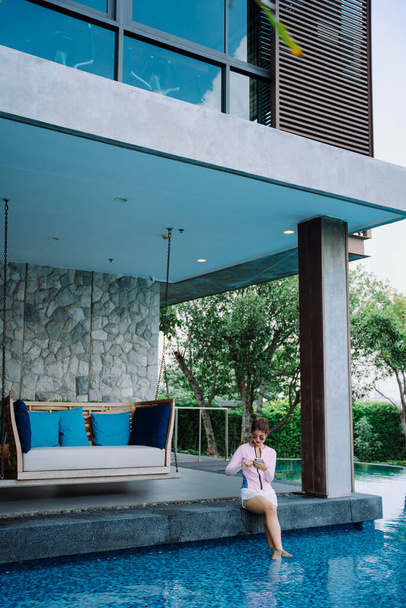 Asian woman traveler wear swim suit using phone at poolside in resort and hotel. - Foto, imagen