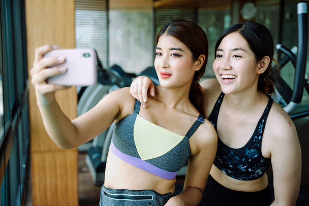 Piękna zdrowa kobieta nosić sportowy biustonosz biorąc selfie ze smartfonem na siłowni. - Zdjęcie, obraz