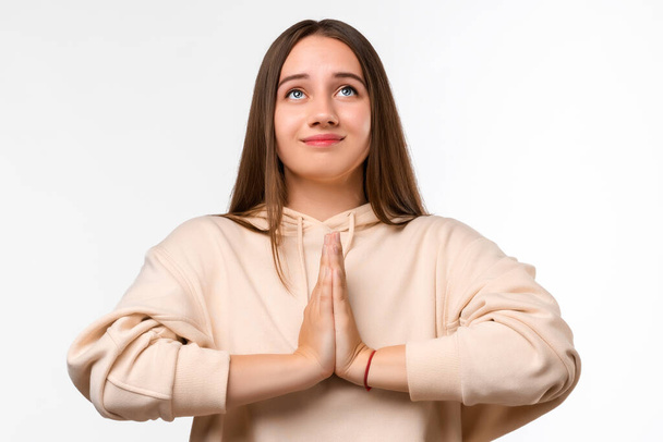 Image of pleased brunette woman with long hair smiling and holding palms together dressed in casual clothes. She meditating, praying for peace and love, having calm and peaceful facial expression - Φωτογραφία, εικόνα