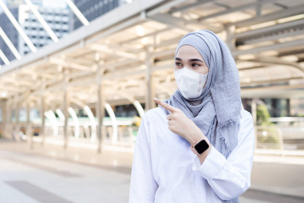 Asiatica musulmana donna d'affari indossa maschera medica per prevenire la polvere e virus infezione, Indicando la strada giusta città. - Foto, immagini