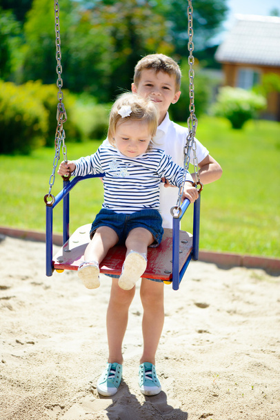 Little brother and sister swinging in summer park  - Foto, imagen