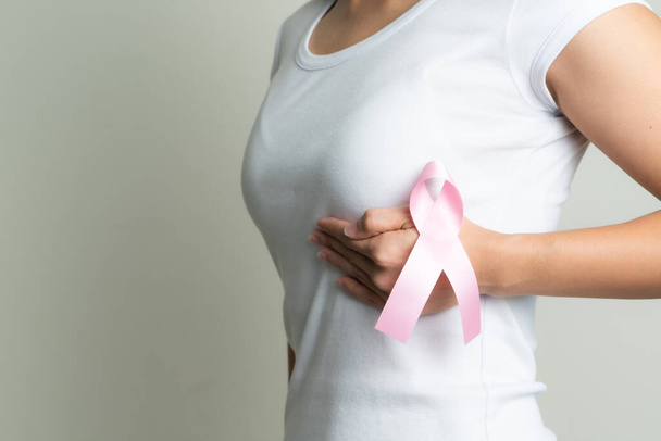 pink badge ribbon on woman hand touching chest to support breast cancer cause. breast cancer awareness concept - Foto, Imagem