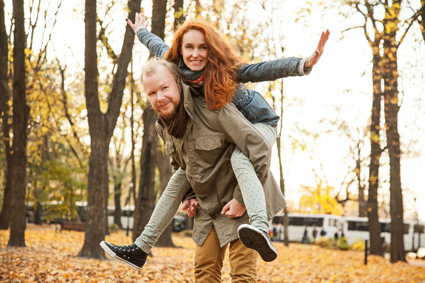 Love story. Autumn Park. Man and woman in a city park tells the story of his love. Happy people having fun. Woman on top of a man on his back. - 写真・画像