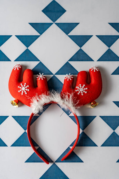 小さな雪の星で飾られた赤いトナカイの角を持つ面白いクリスマスのヘッドバンド、青と白の幾何学的背景、お祝いのクリスマスの背景. - 写真・画像