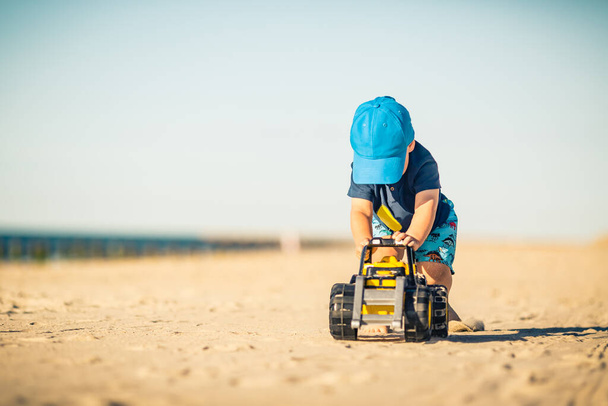 Το αγοράκι παίζει με παιχνίδια σε μια ηλιόλουστη παραλία. Μικρό παιδί που περπατάει στην άμμο. Όμορφη εμπνευσμένη παραλία και θέα στον ωκεανό, τοπίο. - Φωτογραφία, εικόνα
