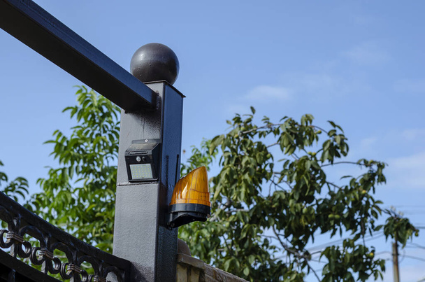Orange siren with solar motion sensor at the entrance gate to a private residence. The upper part of the gate with the fence of the country cottage. Private property. - Photo, Image