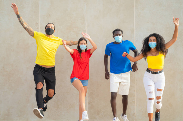 Тысячелетние люди прыгают. Молодые друзья в защитных масках для коронавируса. Вирус и дружба. - Фото, изображение