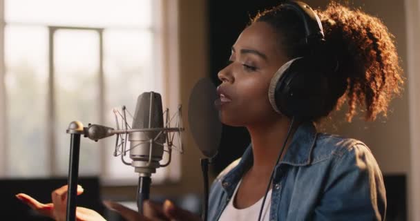 Müzik prodüksiyonu. Afrika kökenli Amerikalı kadın şarkıcının portresi. Ses kayıt stüdyosunda mikrofona şarkı söylüyor. - Video, Çekim