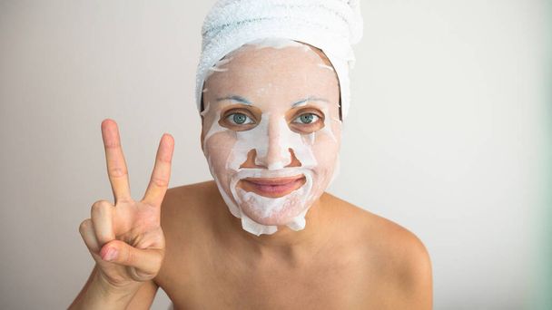 Nainen kääritty valkoinen pyyhe kosmeettinen naamio antaa merkki voitosta tai rauhasta. - Valokuva, kuva