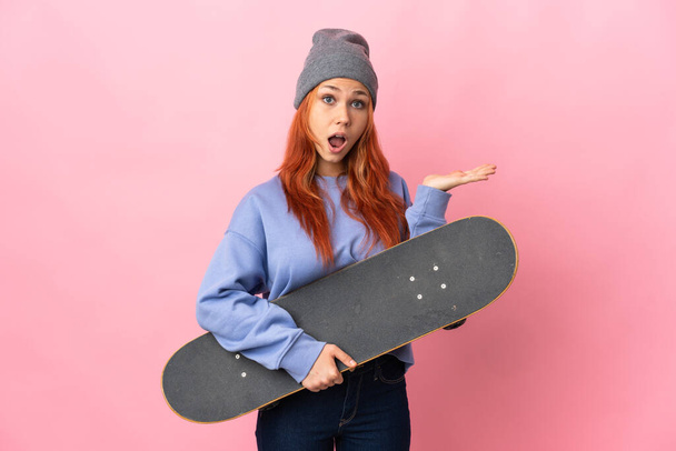 Teenager russische Mädchen isoliert auf rosa Hintergrund mit einem Skate und dabei überraschende Geste - Foto, Bild