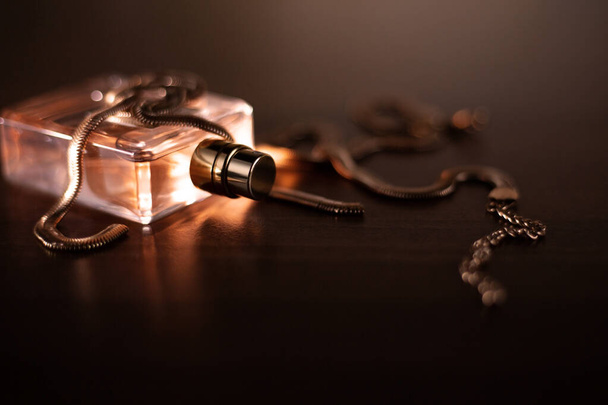 Female perfume and gold necklace on dark background - Foto, afbeelding