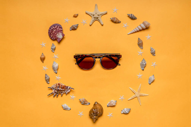Frame made of decorative seashells and sea stars and sunglasses on bright yellow background. Creative composition in minimal style. Summer vacation concept. Flat lay, top view. - Fotografie, Obrázek