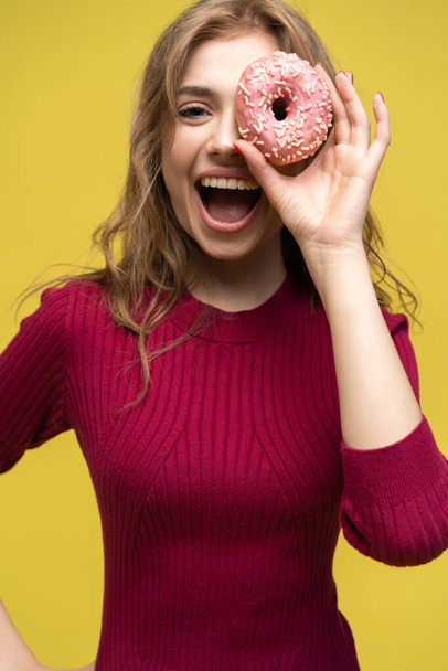 Woman covering her eyes with donut over yellow donut. - Foto, Bild