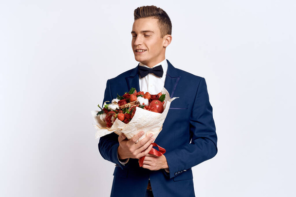 Un hombre elegante en un traje clásico con pajarita lleva un ramo de flores en la mano  - Foto, Imagen