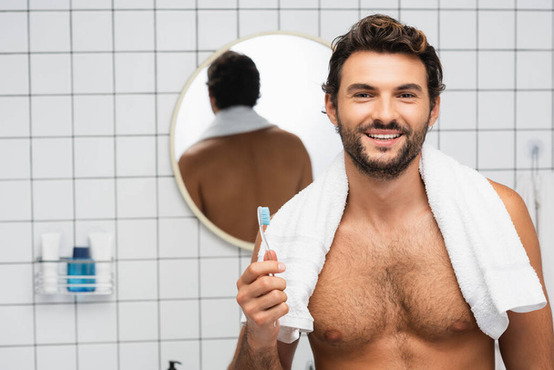 Mosolygó félmeztelen férfi törülközővel a nyakában fogkefével a fürdőszobában  - Fotó, kép