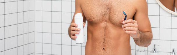 Vista recortada del hombre musculoso sosteniendo espuma de afeitar y afeitadora en el baño, pancarta - Foto, imagen