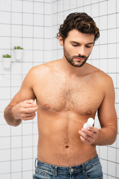 Muscular man holding dental floss in bathroom  - Фото, изображение