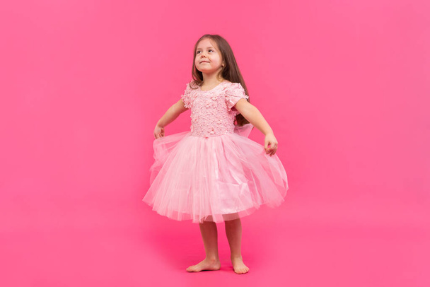 Cute little girl dreams of becoming a ballerina. Little Dancing Girl. Studio Shoot Over Pink Background - Fotografie, Obrázek