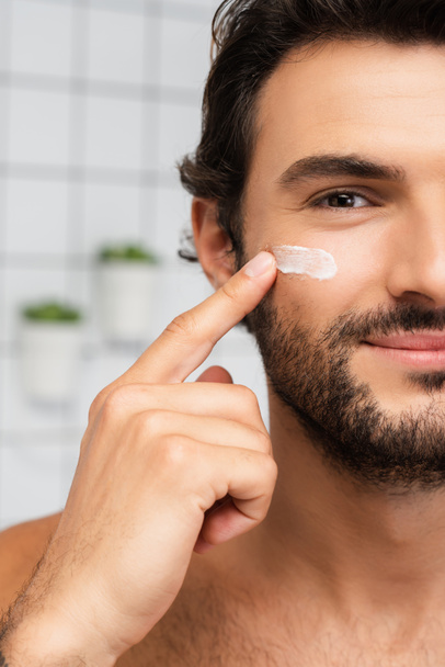 Cropped view of smiling man applying cosmetic cream on cheek  - Foto, immagini