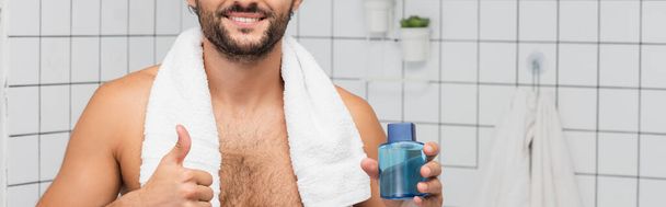 Cropped view of smiling man with towel showing like while holding bottle of after shaving lotion, banner  - Foto, imagen