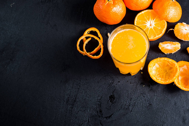 Orange juice in glass with raw oranges on black background. Copy space - Valokuva, kuva