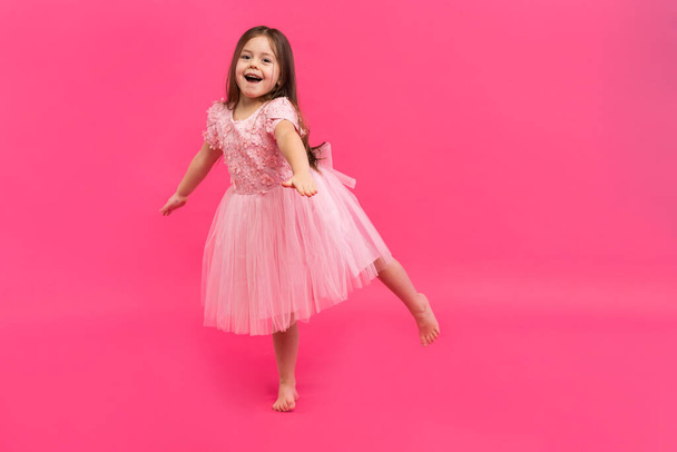 Cute little girl dreams of becoming a ballerina. Little Dancing Girl. Studio Shoot Over Pink Background - Photo, image