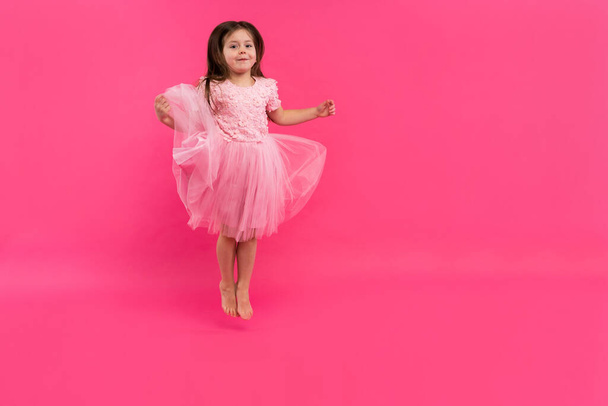 Cute little girl dreams of becoming a ballerina. Little Dancing Girl. Studio Shoot Over Pink Background - Фото, изображение