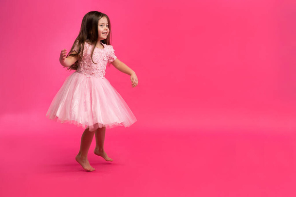 Cute little girl dreams of becoming a ballerina. Little Dancing Girl. Studio Shoot Over Pink Background - Foto, afbeelding