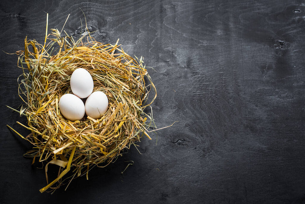 Białe jaja kurze w gnieździe na czarnym tle. Przestrzeń kopiowania - Zdjęcie, obraz