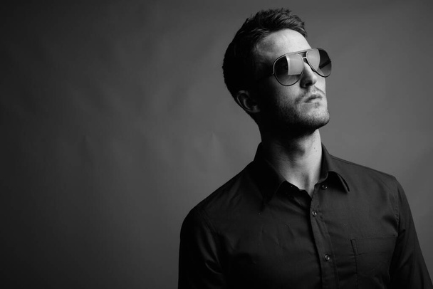 黒と白でグレーの背景にサングラスをかけて若いハンサムなビジネスマンのスタジオショット - 写真・画像