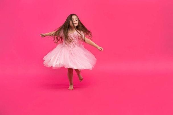 Cute little girl dreams of becoming a ballerina. Little Dancing Girl. Studio Shoot Over Pink Background - Фото, изображение
